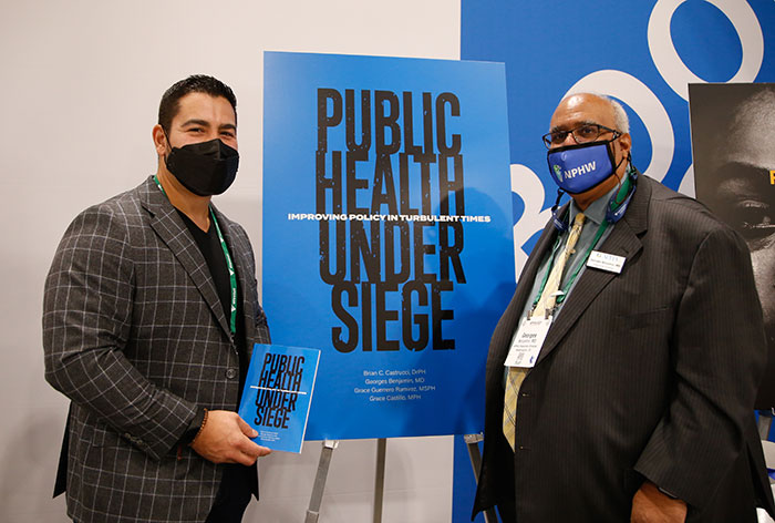 Abdul El-Sayed and Georges Benjamin posing in front of Public Health Under Siege sign