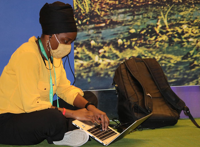 masked woman sitting cross-legged and looking at laptop