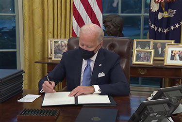 Joe BIden wearing mask and singing papers