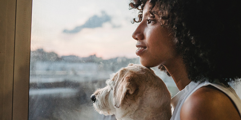 A hopeful woman holds dog while looking out of a window