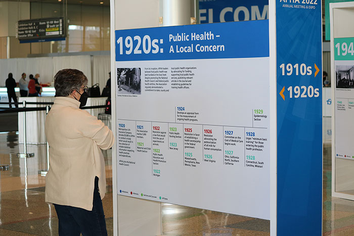 A woman looks at a large sign showcasing public health achievements in the 1920s. 
