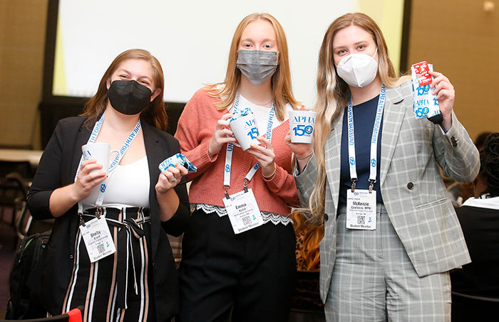 Three student attendees show off their APHA 150th anniversary mug and other swag. 