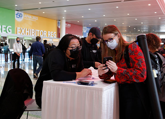 An Annual Meeting attendee shows her COVID-19 vaccine card on her phone to a vaccine checker. 