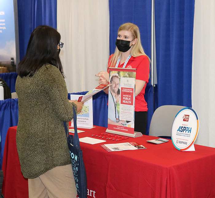 A representative of the Association of Schools and Programs of Public Health talks to an attendee in the expo hall. 