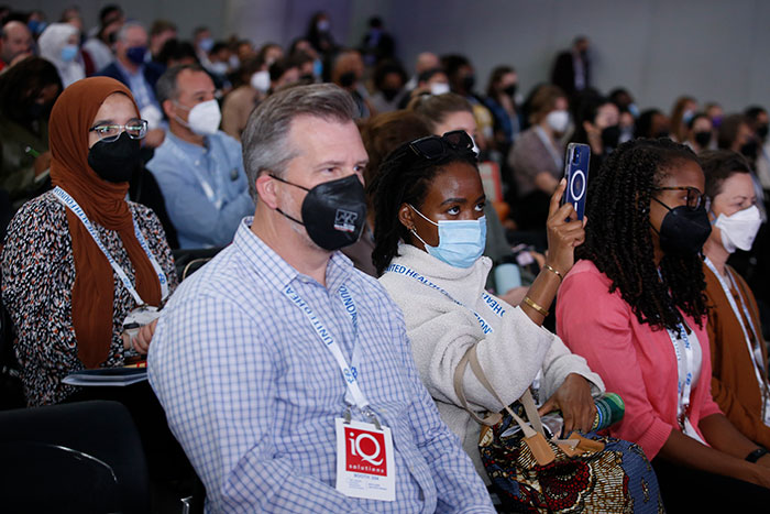 Attendees at the Opening General Session look toward the stage, while one person takes a smartphone photo of the presenter. 