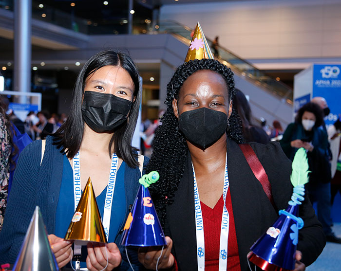 Two attendees hold up the party hats they decorated. 