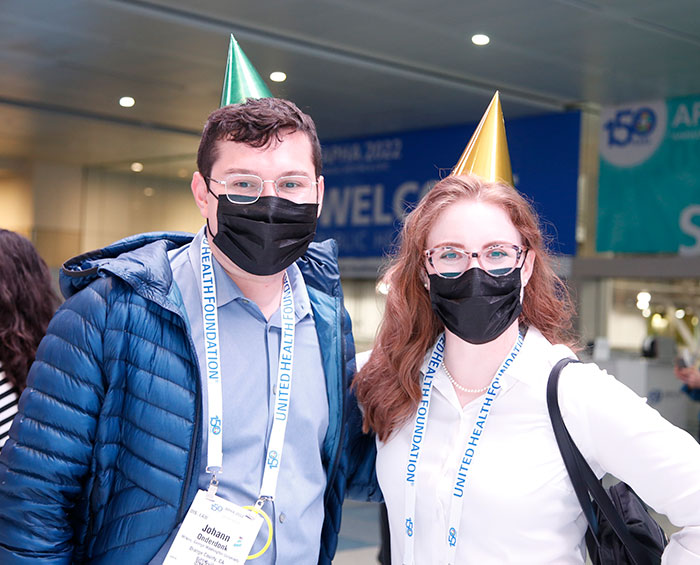 Two young adults wearing masks and party hats pose for the camera. 