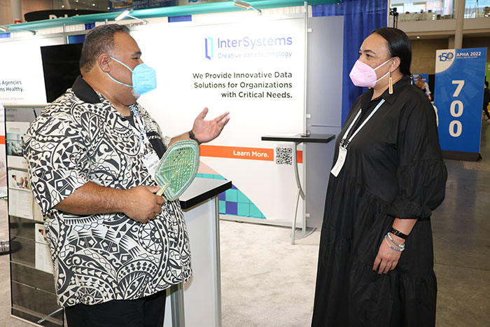 Two attendees stand facing each other in conversation in the expo hall.