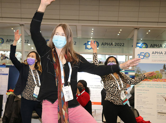 Three women do dance moves, each with their right arm up in the air and their left arm straight out to the side. 