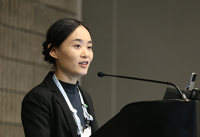 A young Asian woman stands at a lectern.