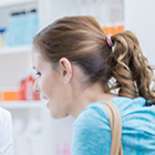 White woman lean on a pharmacy counter to talk to someone.