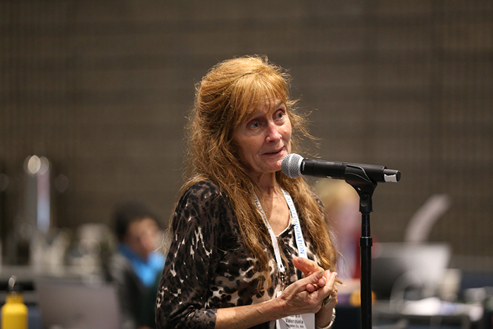Woman with red hair and concerned expression stands at a microphone to ask a question at the Council of Affiliates meeting. 