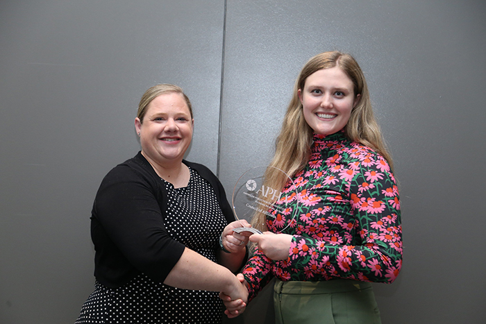 Sarah Rines hands a clear, round glass award to award winner McKenzie Cowlick of the Oklahoma Public Health Association. 