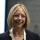 White woman with blonde bob and wearing eyeglasses smiles while talking.