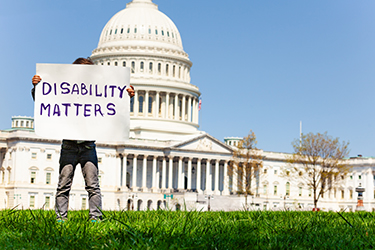 Person stands outside the Capitol holding sign saying "Disability Matters"