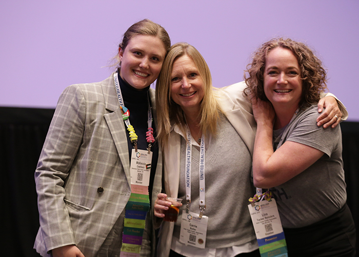 Three women with their arms around each other and smiling pose for the camera. 