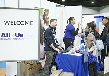 A person answers questions at a booth representing the All of Us Research Program at APHA's Annual Meeting 2022