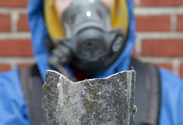 A worker wearing protective gear holds up a piece of asbestos