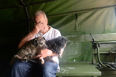 A distressed man holds a hand over his face as two dogs sit on his lap