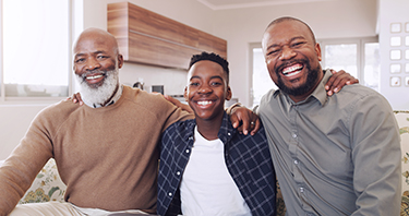 Three generations of Black men laugh with arms wrapped around each other's shoulders
