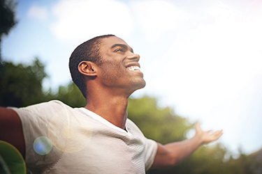 A man outdoors extends his arms out like wings and smiles widely