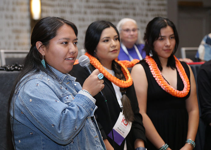 An attendee  holds a microphone and speaks to crowd while two other people stand next to them. 