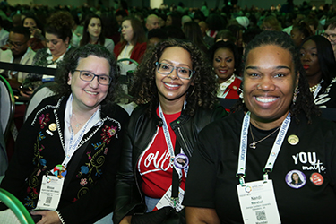 Three women sit next to each other and smile at the camera. 