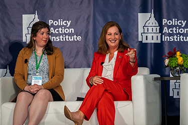 Two people speak while sitting at a sofa during the Policy Action Institute