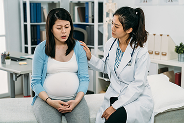 A pregnant woman looks concerned while talking to her doctor.