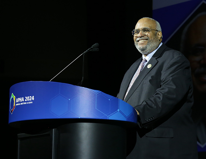 Georges Benjamin stands at a lectern on a dark stage and smiles at the crowd. 
