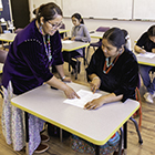 A teacher instructs a student seated at a desk